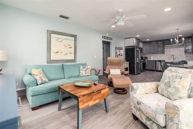 living room with visible vents, baseboards, light wood-style flooring, recessed lighting, and ceiling fan with notable chandelier