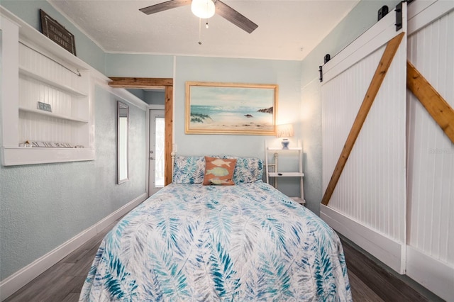 bedroom featuring ceiling fan, baseboards, wood finished floors, a barn door, and a textured wall