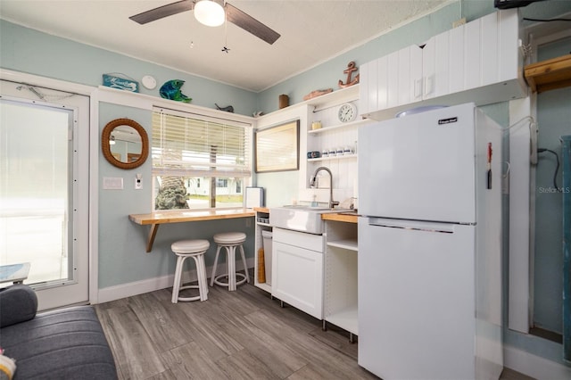 kitchen featuring a wealth of natural light, a sink, open shelves, wood finished floors, and freestanding refrigerator