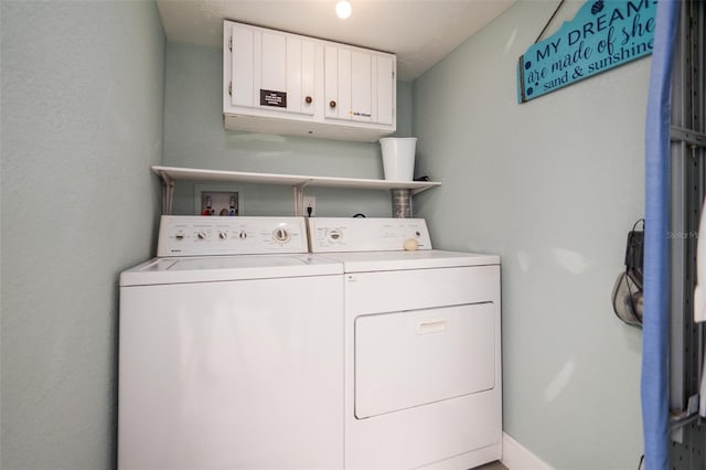 clothes washing area featuring separate washer and dryer, cabinet space, and baseboards