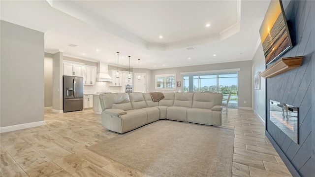 living room with a raised ceiling, recessed lighting, crown molding, and baseboards