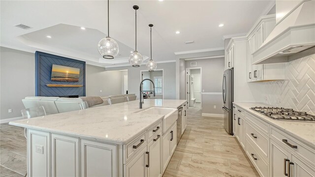 kitchen featuring premium range hood, visible vents, an island with sink, a sink, and stainless steel appliances