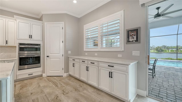 kitchen with crown molding, ceiling fan, a water view, stainless steel double oven, and white cabinets