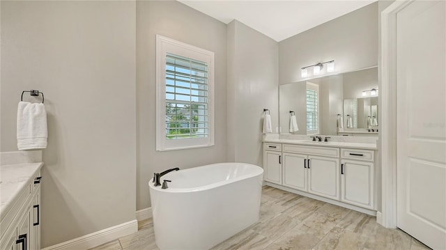 full bathroom featuring baseboards, plenty of natural light, a soaking tub, and vanity