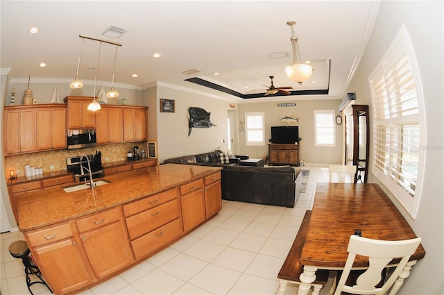 kitchen featuring stainless steel microwave, a sink, a tray ceiling, decorative backsplash, and a kitchen island with sink