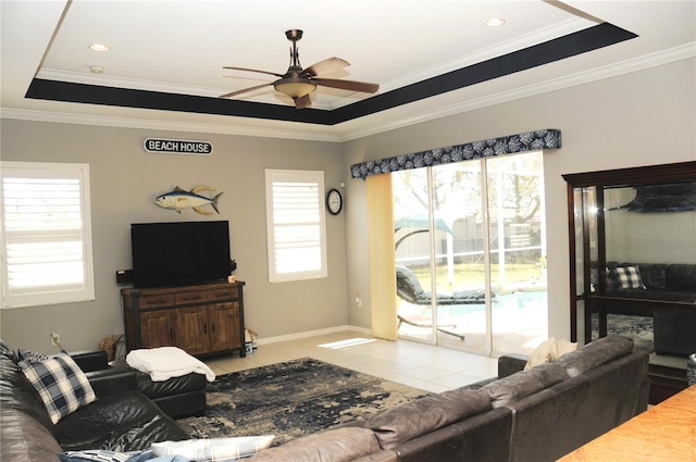 living room with tile patterned floors, a raised ceiling, ornamental molding, baseboards, and ceiling fan