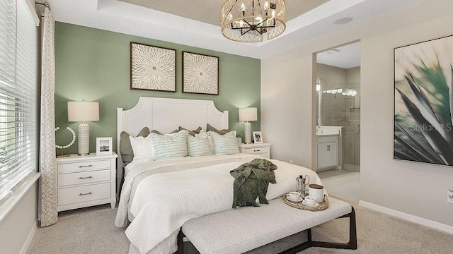 bedroom featuring light carpet, baseboards, a raised ceiling, ensuite bath, and an inviting chandelier