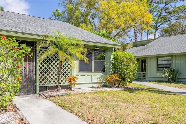 doorway to property featuring a yard, a shingled roof, and board and batten siding