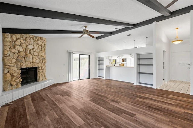 unfurnished living room featuring wood finished floors, ceiling fan, a stone fireplace, vaulted ceiling, and a textured ceiling