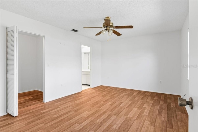 empty room featuring light wood-type flooring, a ceiling fan, visible vents, and a textured ceiling