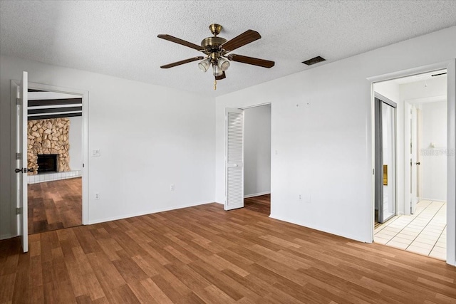 unfurnished bedroom featuring a textured ceiling, visible vents, wood finished floors, and a stone fireplace