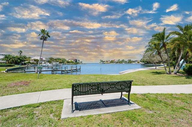 view of home's community with a yard, a water view, boat lift, and a boat dock