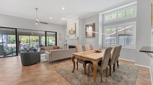 dining space featuring baseboards, a tiled fireplace, ornamental molding, light tile patterned floors, and a ceiling fan