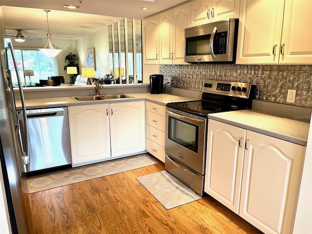 kitchen featuring a sink, stainless steel appliances, pendant lighting, light wood-type flooring, and backsplash