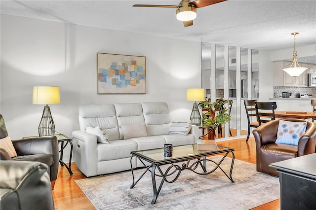 living room featuring a textured ceiling, light wood-type flooring, and a ceiling fan