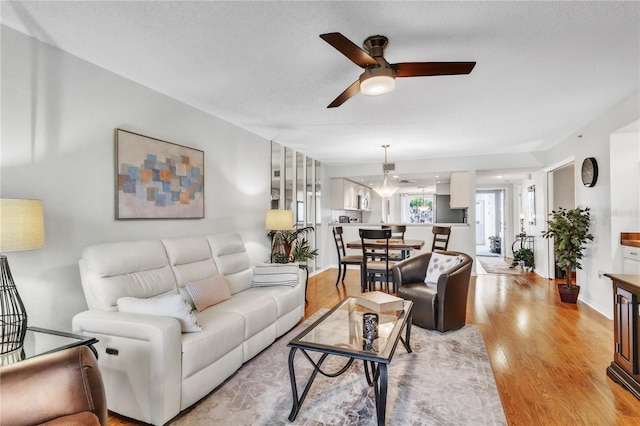 living area featuring a ceiling fan, baseboards, light wood finished floors, and a textured ceiling