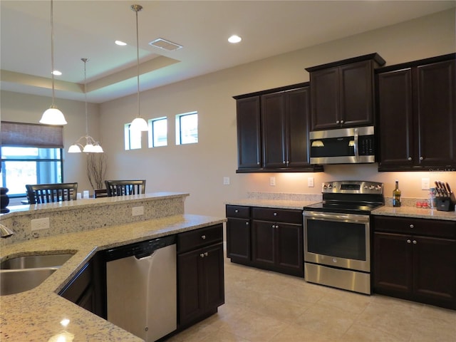 kitchen featuring pendant lighting, a sink, a tray ceiling, appliances with stainless steel finishes, and light stone countertops