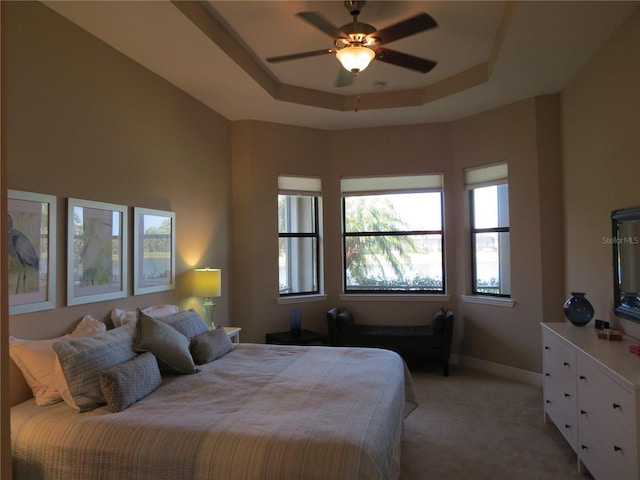 bedroom with a tray ceiling, baseboards, light colored carpet, and ceiling fan