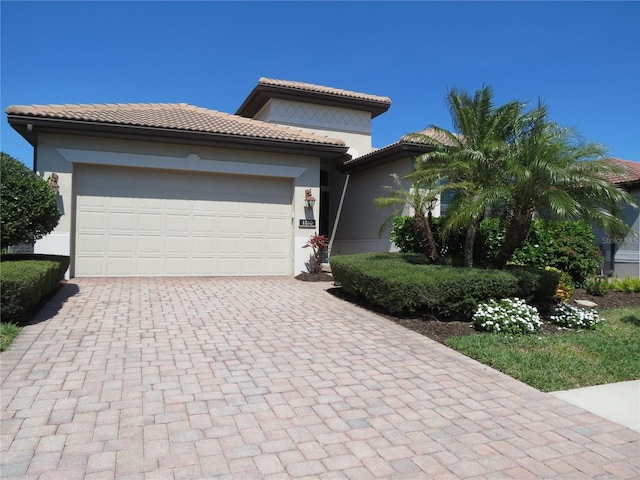 view of front facade with stucco siding, a tiled roof, decorative driveway, and a garage