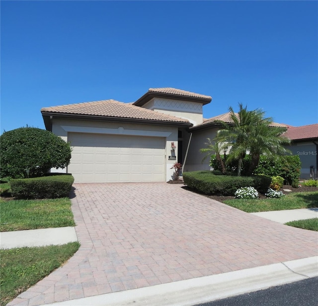 prairie-style home featuring decorative driveway, a tiled roof, an attached garage, and stucco siding