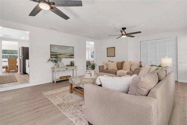 living room with a ceiling fan, light wood-style flooring, a healthy amount of sunlight, and baseboards