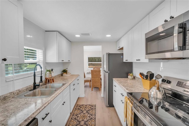 kitchen with visible vents, light wood finished floors, a sink, stainless steel appliances, and white cabinetry