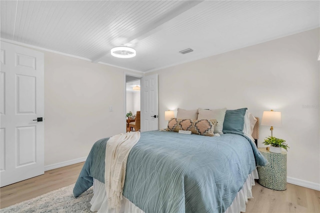 bedroom featuring visible vents, light wood-type flooring, baseboards, and ornamental molding