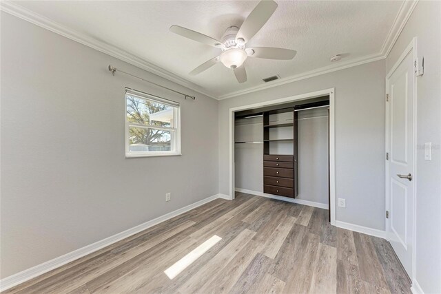 unfurnished bedroom featuring light wood-type flooring, visible vents, ornamental molding, a closet, and baseboards