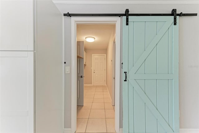 hall featuring light tile patterned floors, baseboards, and a barn door