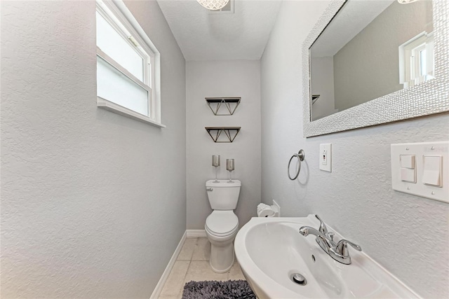 bathroom with a textured wall, baseboards, toilet, and tile patterned flooring