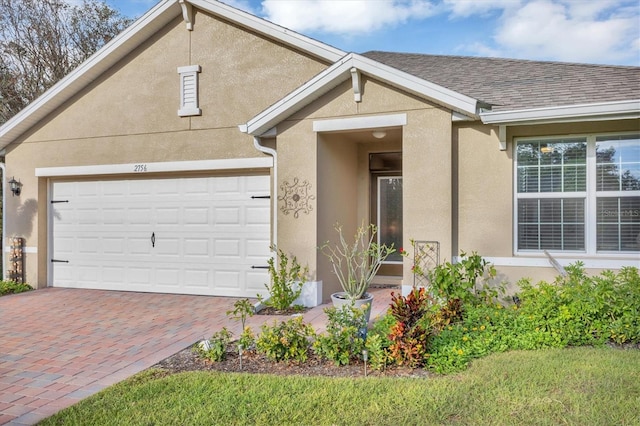 view of front of property featuring a garage, a shingled roof, decorative driveway, and stucco siding