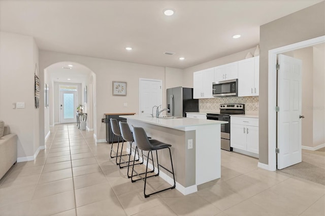 kitchen featuring arched walkways, stainless steel appliances, a sink, a kitchen bar, and a center island with sink