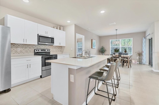 kitchen with stainless steel appliances, a sink, white cabinetry, backsplash, and an island with sink