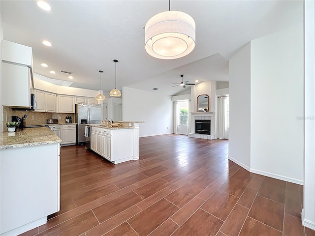 kitchen featuring stainless steel appliances, dark wood-type flooring, a tiled fireplace, open floor plan, and backsplash