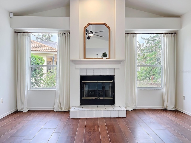 unfurnished living room featuring baseboards, wood finished floors, a tile fireplace, and vaulted ceiling