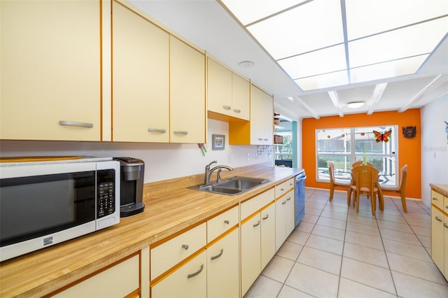 kitchen featuring white microwave, dishwasher, light tile patterned floors, cream cabinets, and a sink