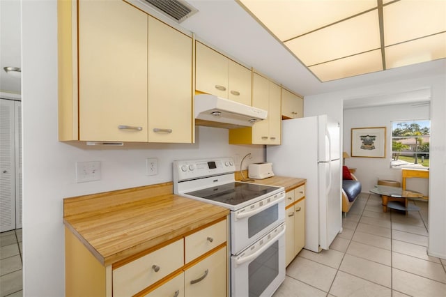 kitchen with cream cabinetry, under cabinet range hood, wood counters, white appliances, and light tile patterned floors