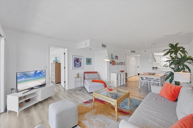 living room with light wood finished floors, visible vents, and a textured ceiling