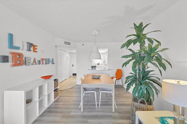 dining area featuring a textured ceiling, visible vents, and light wood-type flooring