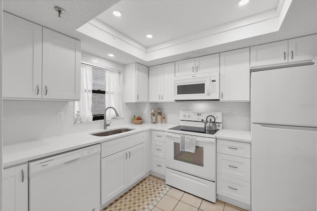 kitchen with white appliances, white cabinetry, a tray ceiling, and a sink