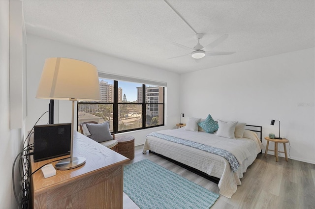 bedroom with ceiling fan, baseboards, a textured ceiling, and light wood-style flooring