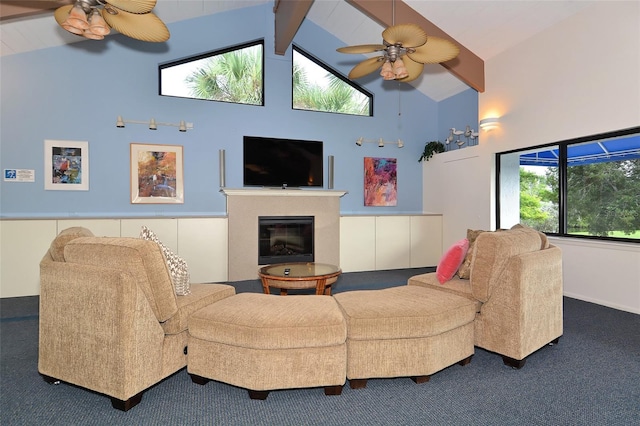 living area featuring carpet, ceiling fan, beam ceiling, a glass covered fireplace, and high vaulted ceiling