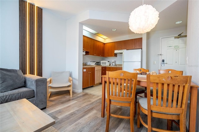 kitchen featuring light wood finished floors, under cabinet range hood, light countertops, freestanding refrigerator, and brown cabinetry