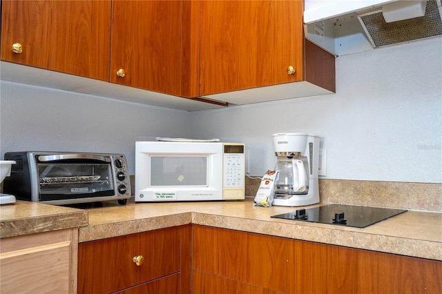 kitchen featuring white microwave, a toaster, light countertops, under cabinet range hood, and black electric cooktop