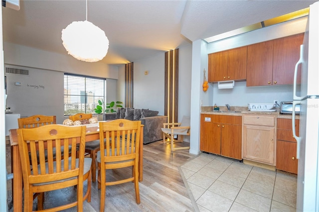 kitchen with visible vents, light countertops, freestanding refrigerator, light wood-style floors, and a sink