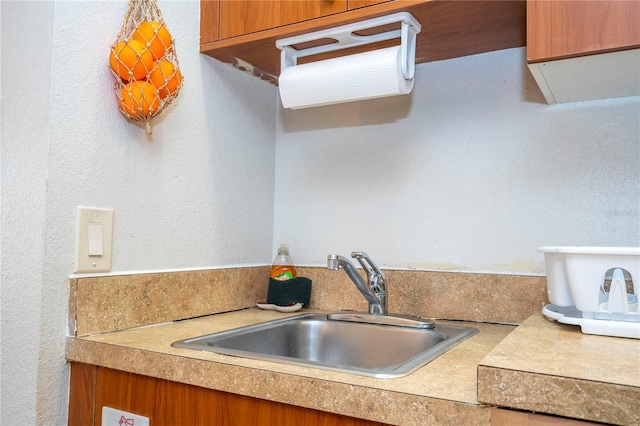 kitchen featuring a sink, brown cabinets, a textured wall, and light countertops