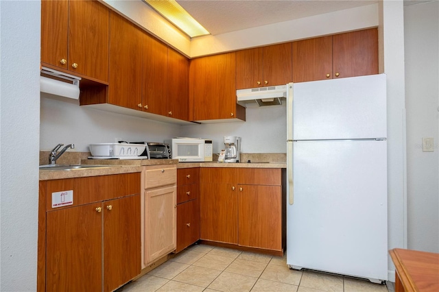 kitchen featuring under cabinet range hood, light countertops, light tile patterned floors, white appliances, and a sink