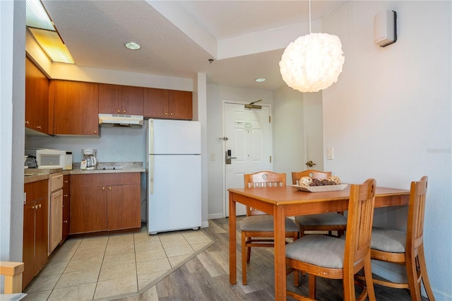 kitchen with white appliances, light wood-type flooring, light countertops, under cabinet range hood, and brown cabinets