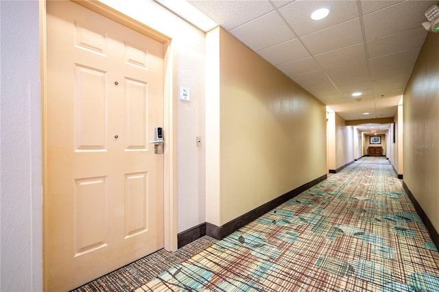 hall featuring a paneled ceiling and baseboards