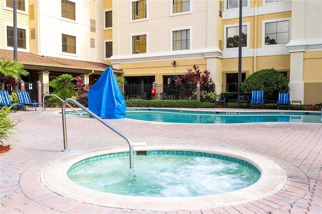 pool with a patio area, fence, and a hot tub